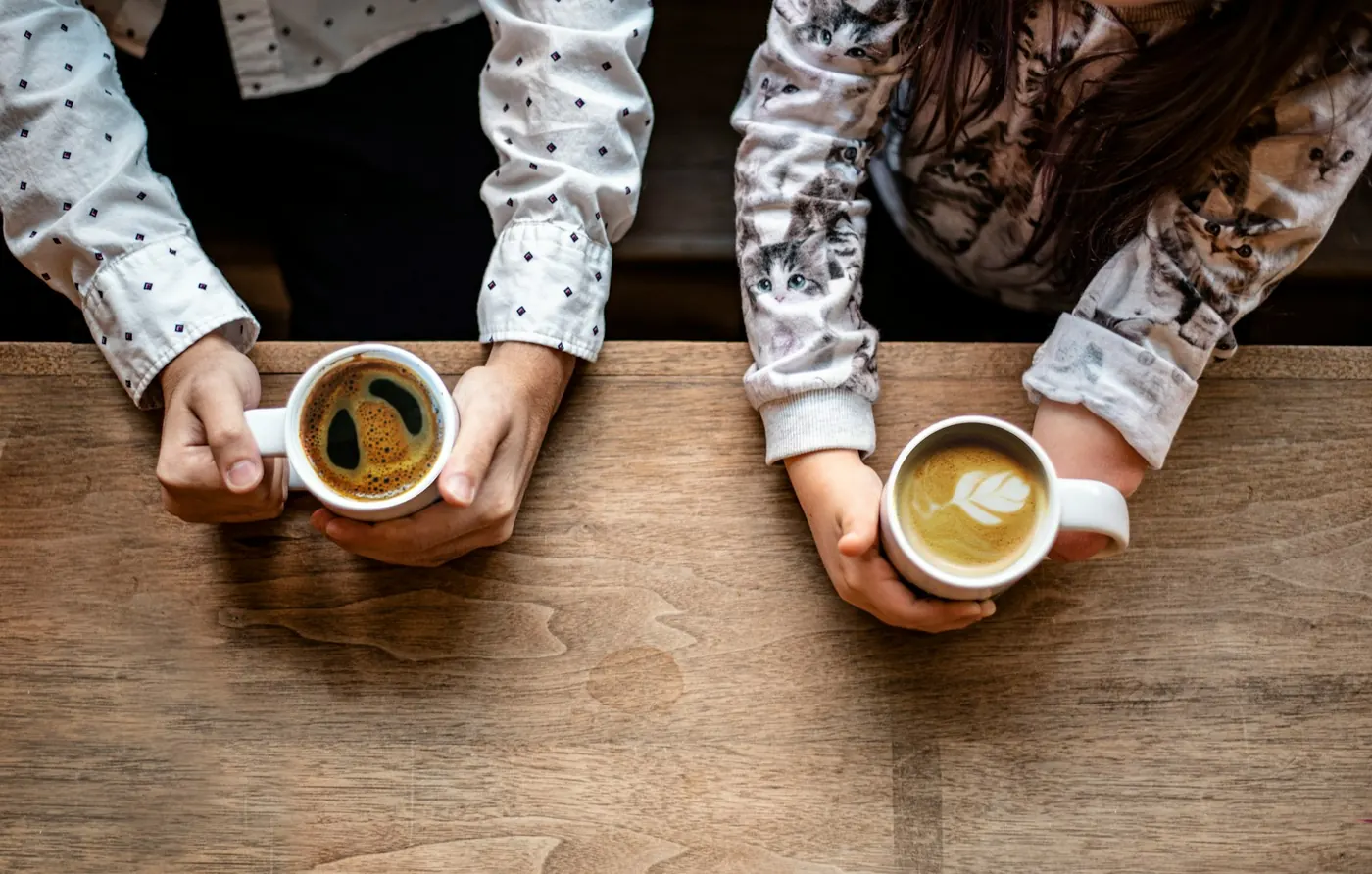 Duas pessoas segurando xícaras de café sobre uma mesa de madeira