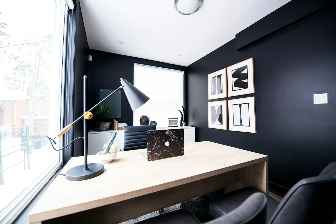 Escritório com parede escura, mesa de madeira e luminária