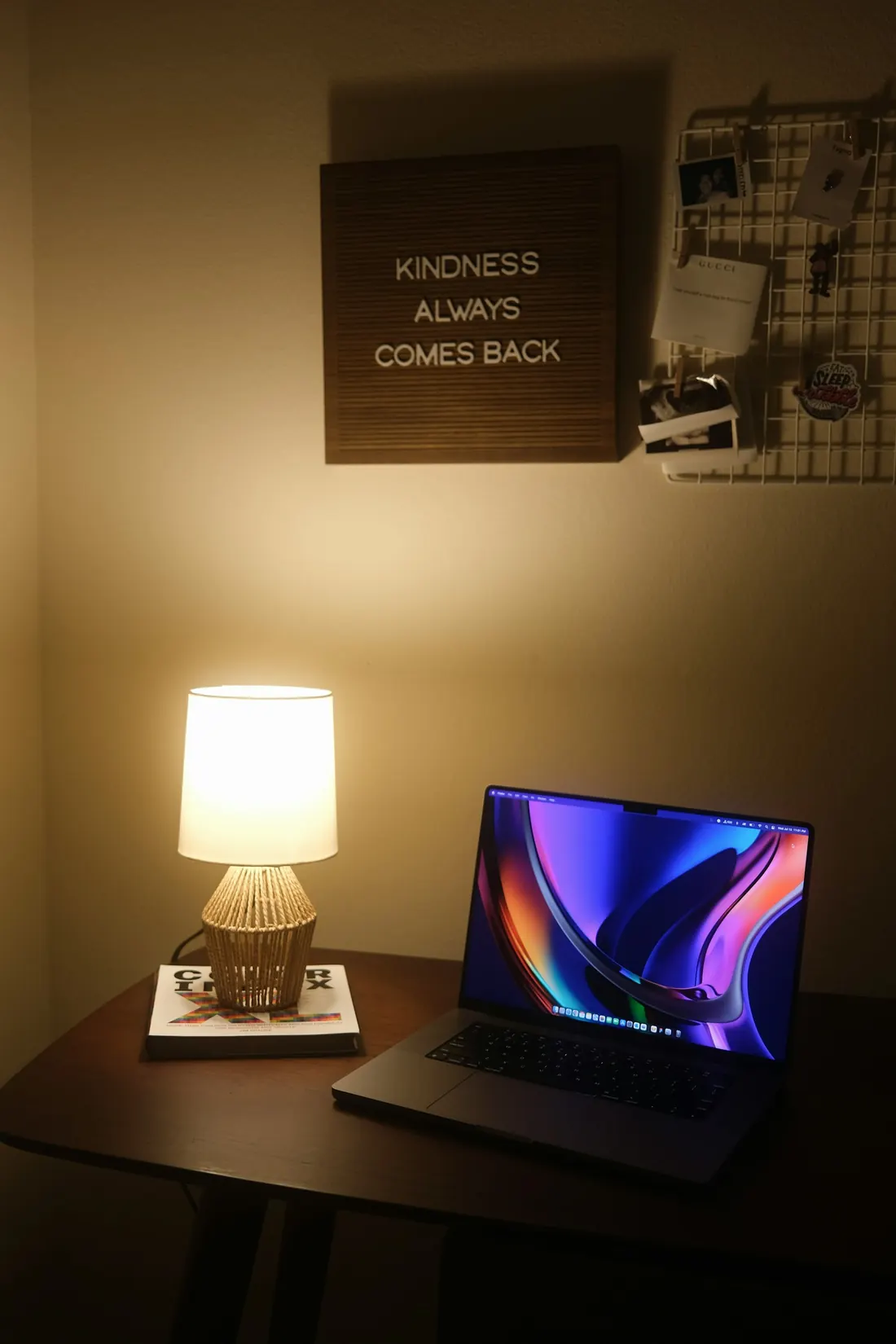 Notebook aberto ao lado de um abajur aceso em uma mesa, à noite